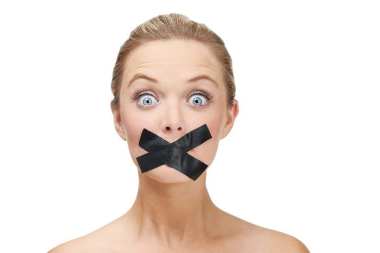 Silenced by the system. A young blonde woman looking shocked with duct tape covering her mouth.